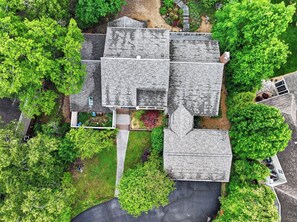 An aerial view of a residential area with multiple houses, a central paved area, and surrounding greenery.