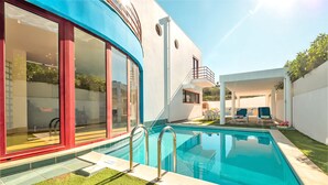 Ein modernes Haus mit Swimmingpool, großen Fenstern und einer überdachten Sitzterrasse.