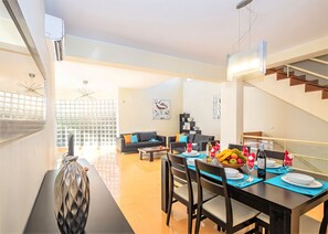 A modern dining area with a table set for two, a sofa, and a staircase.