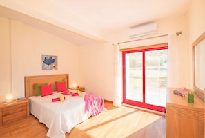 A bedroom with a bed, nightstands, a painting, a window with a view, and a wooden dresser.