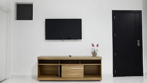 A modern room with a wooden TV stand, a flat-screen TV, a small window, and a black door.