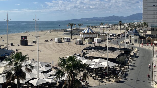 Une zone aménagée au bord de la plage, avec un carrousel, des palmiers et des espaces de détente en plein air sous des parasols.
