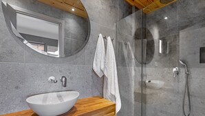 A modern bathroom with a wooden vanity, a white vessel sink, a glass-enclosed shower, and a round mirror. - Messinian Riviera Villas (Petalidi)