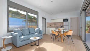 A modern living room with a sofa, coffee table, and dining area with chairs. - Messinian Riviera Villas (Petalidi)