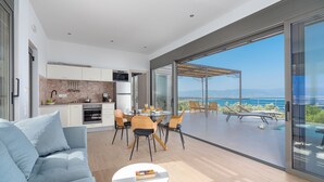 A modern kitchen with a dining area and a large sliding glass door leading to a poolside. - Messinian Riviera Villas (Petalidi)