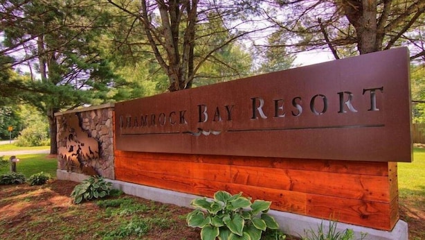 A sign for Shamrock Bay Resort with a stone and wood design, surrounded by greenery.