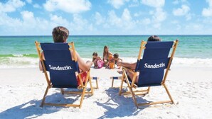 Two beach chairs with "Sandestin" branding on the backrests, positioned on a sandy beach with the ocean in the background. - Beachy Sandestin studio, walk to Baytowne Wharf (Miramar Beach)
