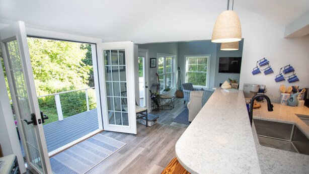 Een moderne keuken met een groot eiland, een eethoek met een blauwe stoel en uitzicht op de omgeving via glazen deuren.