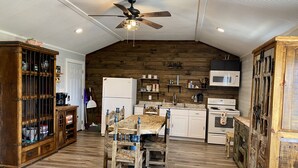 A rustic kitchen with wooden walls, a wooden dining table, and a ceiling fan. -  Secluded Casita on the Crystal Clear Nueces River (Uvalde)