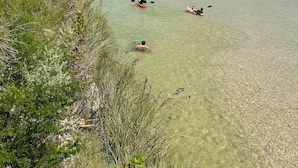 A river with kayaks, surrounded by greenery and a white sandy beach. -  Secluded Casita on the Crystal Clear Nueces River (Uvalde)