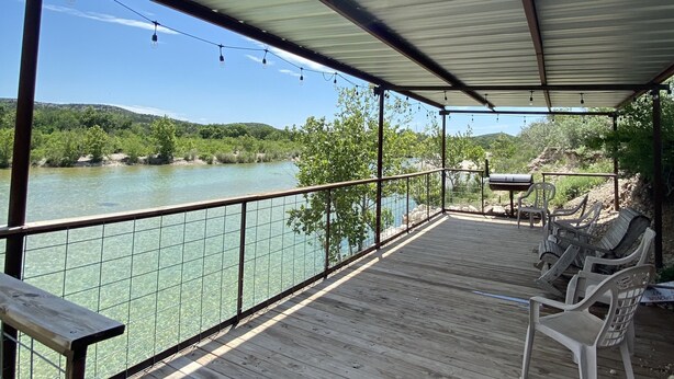 A wooden deck with a metal roof, overlooking a body of water and greenery. -  Secluded Casita on the Crystal Clear Nueces River (Uvalde)