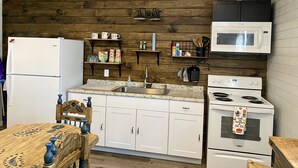 A kitchen with white cabinets, a wooden ceiling, a microwave, a stove, and shelves with kitchen items. -  Secluded Casita on the Crystal Clear Nueces River (Uvalde)