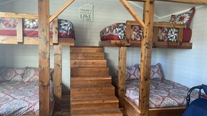 A cabin interior with wooden bunk beds, a staircase, and a sign that reads "THERE'S NO PLACE LIKE the cabin". -  Secluded Casita on the Crystal Clear Nueces River (Uvalde)