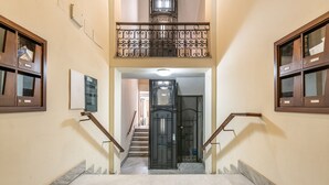 Ein mehrgeschossiges Interieur mit Marmorböden, einer zentralen Treppe und einem Balkon mit schmiedeeisernen Geländern.