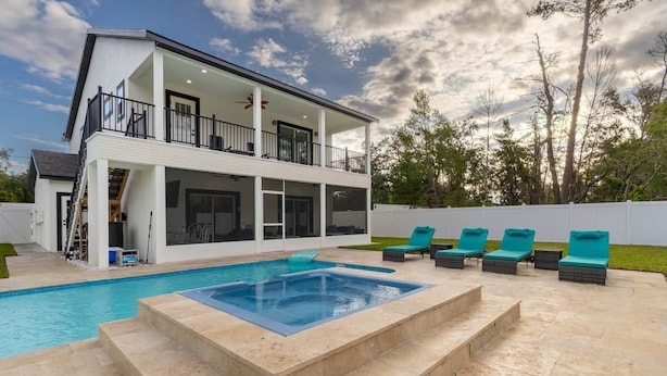 A two-story house with a swimming pool, outdoor seating, and a white exterior.