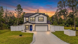 A two-story house with a garage, surrounded by a fence, and a driveway leading to the entrance.