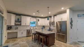 A modern kitchen with white cabinets, a central island with stools, stainless steel appliances, and pendant lighting.