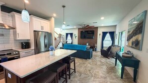 A modern kitchen with a central island, a dining area with a sofa, and a living room with a TV and seating.