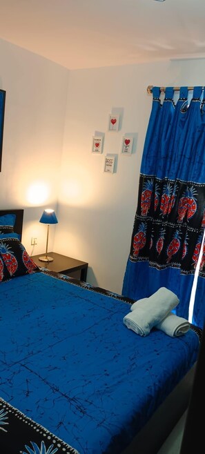 Ein Schlafzimmer mit Bett, Nachttisch, Lampe und Vorhang mit Ananasmuster.