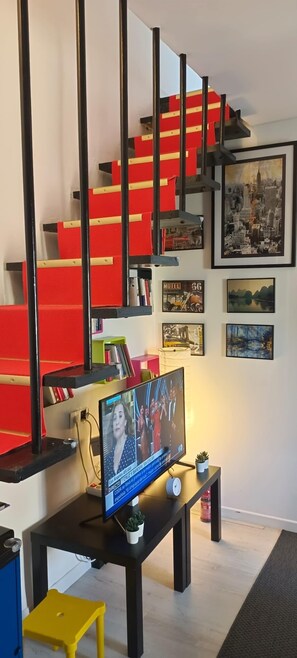 A modern living room with a red and black staircase, a flat-screen TV on a black stand, and various framed pictures on the wall. - Luxury Apartment "Ma Suk (Alicante (Alacant))