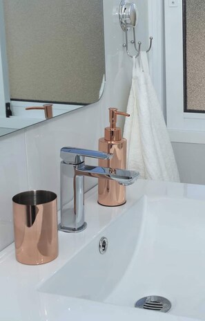 Ein Badezimmer mit einem weißen Waschbecken, einem Kupferarmaturen und einem Spiegel darüber.
