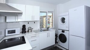 Een moderne keuken met witte kasten, een magnetron, een waterkoker en een wasmachine.