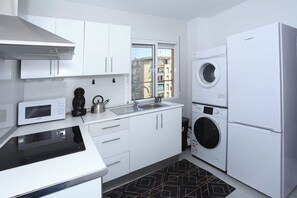 Une cuisine moderne avec des meubles blancs, un four à micro-ondes, une bouilloire et un lave-linge.