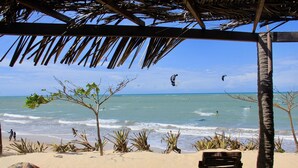 A beach with a wooden bench and a thatched roof structure. - Beach Front Exclusive Villa with Pool (SAO MIGUEL DO GOSTOSO)