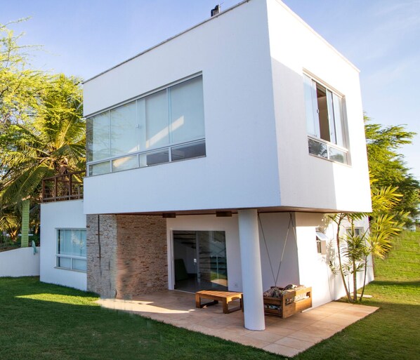 Una casa moderna de dos pisos con grandes ventanales, fachada de piedra y un pequeño espacio al aire libre para sentarse.