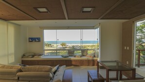 A modern living room with a large window overlooking a beach, a sofa, a coffee table, and a dining table. - Beach Front Exclusive Villa with Pool (SAO MIGUEL DO GOSTOSO)