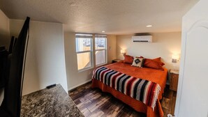 Un dormitorio con una cama grande, dos lámparas de noche, un ventanal y un aire acondicionado.