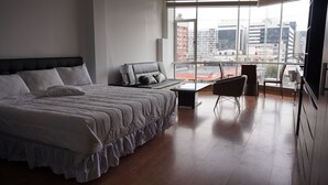 Ein modernes Schlafzimmer mit einem großen Bett, einer Sitzecke, einem Esstisch und Blick auf die Stadt durch große Fenster.