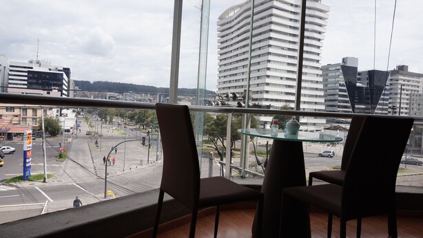 Blick aus einem Fenster mit zwei Stühlen und einem Glastisch auf eine Stadtansicht mit modernen Gebäuden und einer belebten Straße.