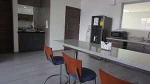Eine moderne Küche mit einer Granit Arbeitsplatte, Edelstahlgeräten und Holzschränken. Zwei Barhocker mit blauen Kissen sind vorhanden.