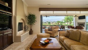 A spacious living room with a large TV, comfortable seating, a fireplace, and a view of the outdoors. - La Quintuta -- our home away from home (La Quinta)