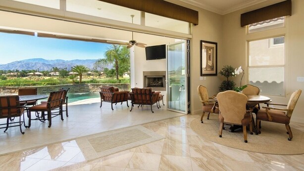 A spacious living area with a large glass door leading to a pool, a fireplace, and a dining area with chairs and a table. - La Quintuta -- our home away from home (La Quinta)