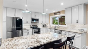 A modern kitchen with white cabinets, stainless steel appliances, a marble countertop, and pendant lighting. - Lofted Bluff Sunset Lake Views and Private Boat Dock (Osage Beach)