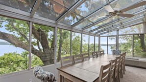 A conservatory with a dining table and chairs, large windows, and a ceiling fan. - Lofted Bluff Sunset Lake Views and Private Boat Dock (Osage Beach)