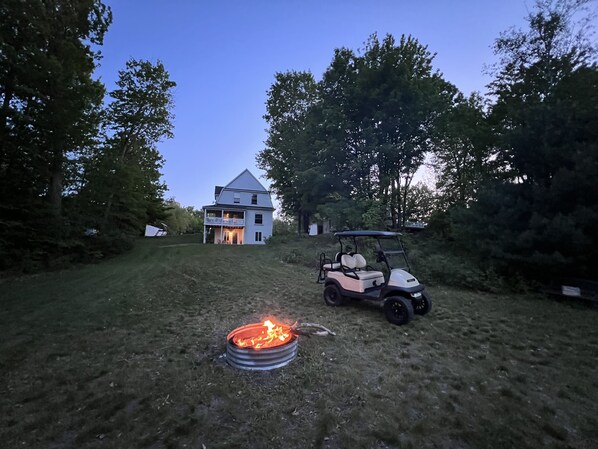 Ein Haus mit einem zweistöckigen Balkon, einer Feuerstelle und einem Golfwagen auf dem Grundstück.