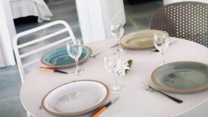 A dining table set with plates, cutlery, and wine glasses, with a bed and a chair visible in the background. - Cottage Papaya Moorea (Moorea-Maiao)