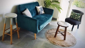 A teal sofa with wooden legs, a round wooden stool, and a black chair with a green cushion. - Cottage Papaya Moorea (Moorea-Maiao)