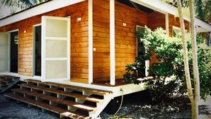 A wooden cabin with a porch, a staircase, and a small garden area. - Cottage Papaya Moorea (Moorea-Maiao)