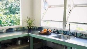 A compact kitchen with a built-in washing machine, a sink, and a window with open blinds. - Cottage Papaya Moorea (Moorea-Maiao)