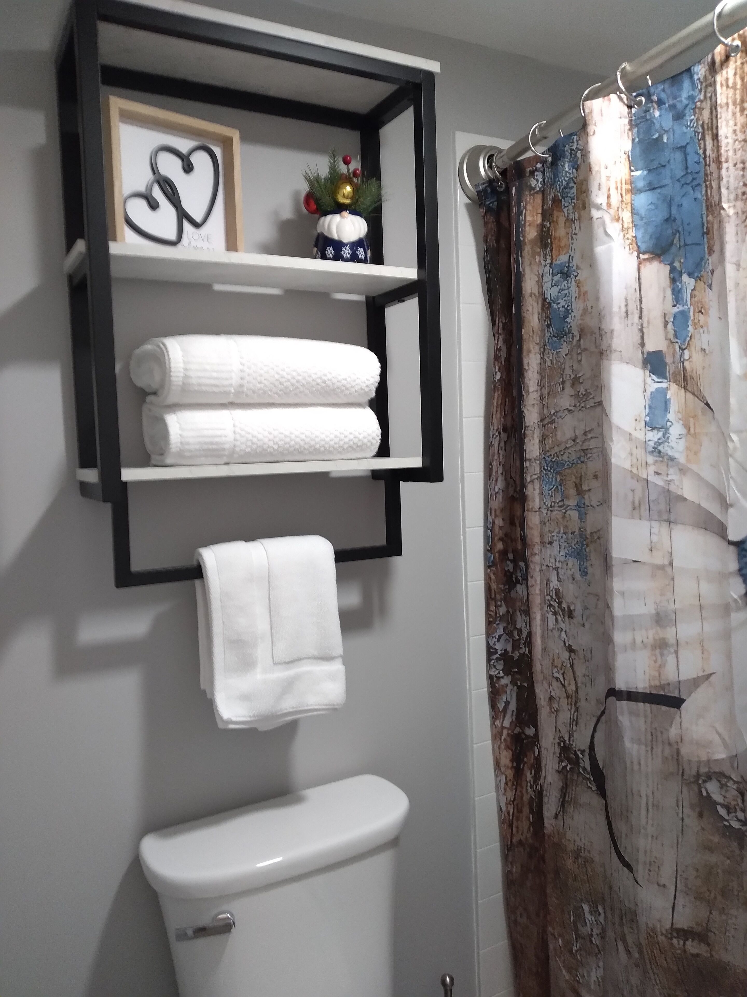 A bathroom with a toilet, a shelf with towels, and a shower curtain.
