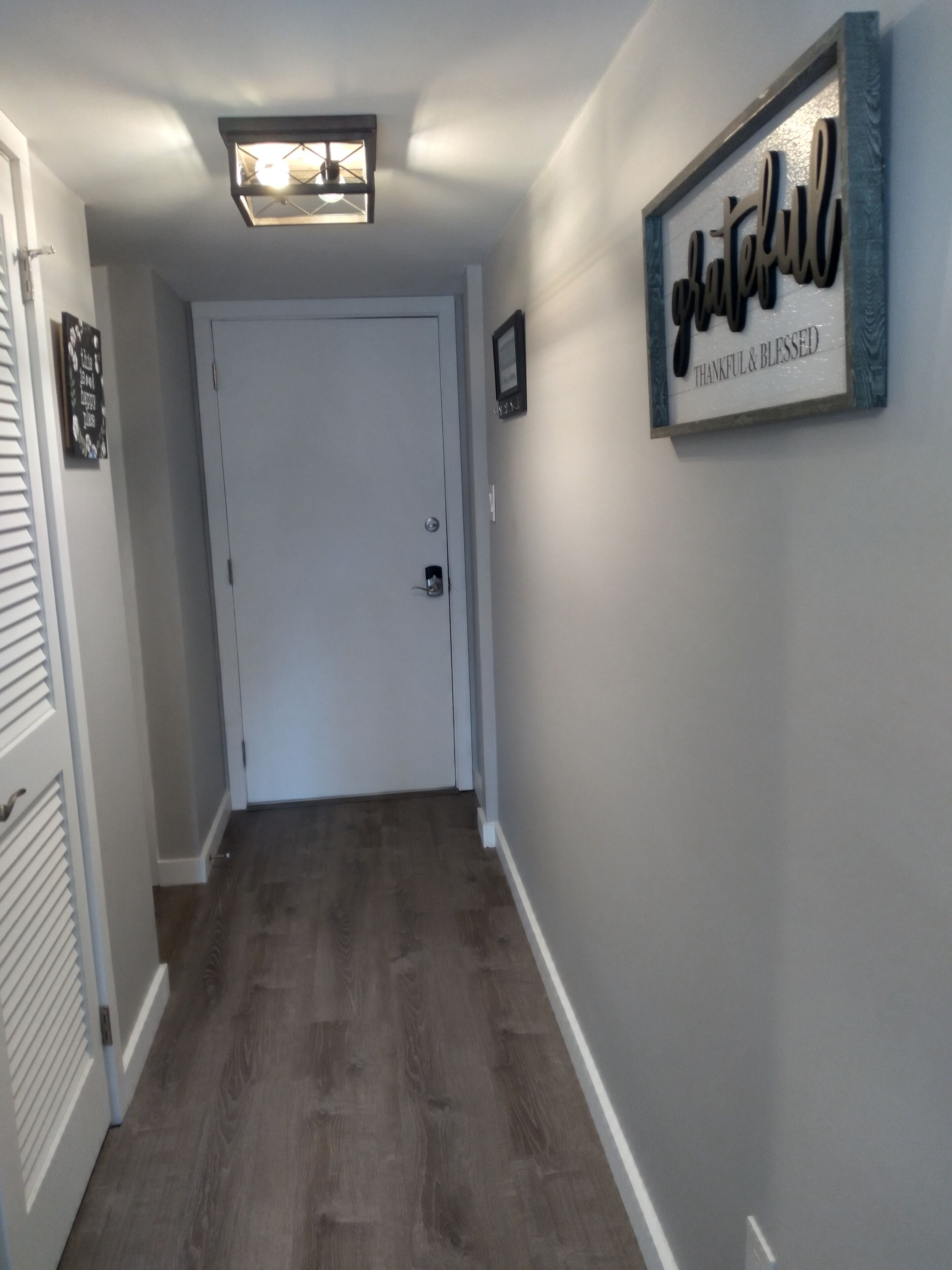 Un pasillo con piso de madera, una puerta blanca y un letrero en la pared que dice 'thankful & blessed'.