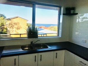 Enjoy a sea view from this kitchen with a double sink, countertop, and white cabinets.