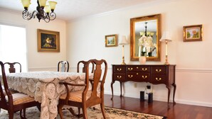 Un comedor con una mesa dispuesta para cuatro personas, rodeada de sillas, un aparador de madera con cajones y un espejo grande sobre el aparador.
