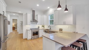 A modern kitchen with white cabinetry, stainless steel appliances, and a large island with bar stools. - Luxurious Living in Old Town Bluffton! Sleeps 6! Prime Location! (Bluffton)