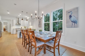 A spacious kitchen with a dining area, large windows, and a chandelier.