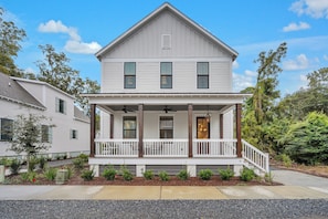 A two-story house with a front porch, a small garden, and a clear blue sky.